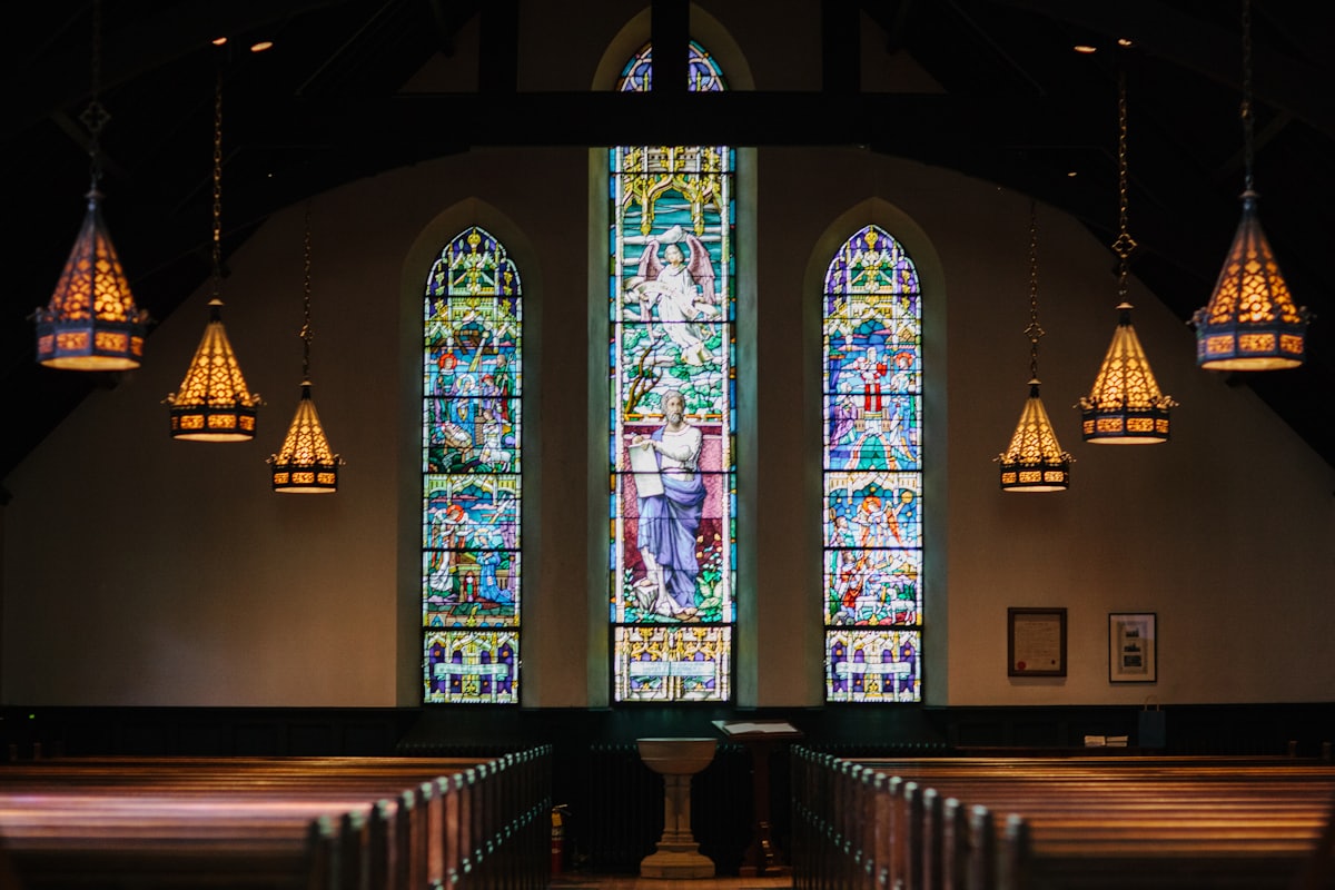 Interno di una chiesa con vetrate colorate illuminate dalla luce e file di banchi in legno